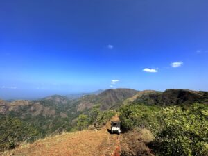 Scenic mountain road with a jeep driving towards the ocean, capturing the essence of Vagamon’s adventurous trekking trails and off-road vehicle tourism, in Kerala, India