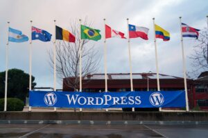 A row of nine flags representing different countries, including Argentina, Australia, Belgium, Brazil, Canada, Chile, Columbia, Costa Rica, are displayed on tall poles against a backdrop of a building with solar panels on the roof. A large blue banner with the word “WordPress” is positioned below the flags.